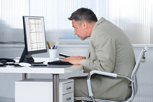 An office worker with an exaggerated forward head posture and round back working in front of a computer